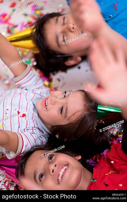 Happy kids celebrating party with blowing confetti while lying on the floor