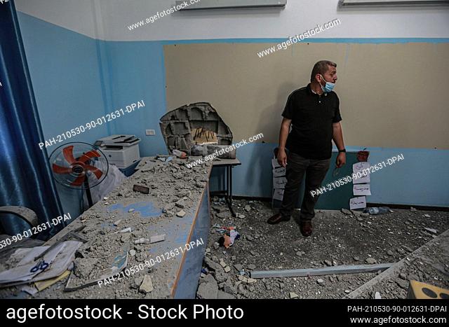 30 May 2021, Palestinian Territories, Gaza City: An employee of the Palestinian Ministry of Education inspects a hole in the wall of a damaged classroom at a...