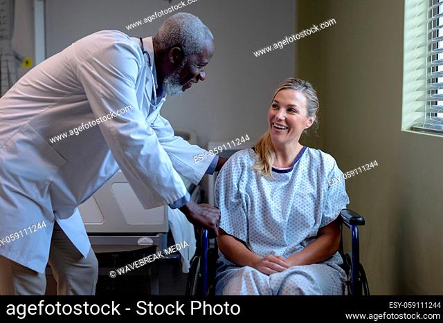 Diverse male doctor and female patient sitting on wheelchair smiling to each other