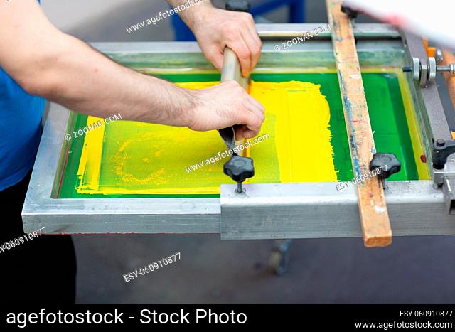 Serigraphy silk screen print process at clothes factory. Frame, squeegee and plastisol color paints