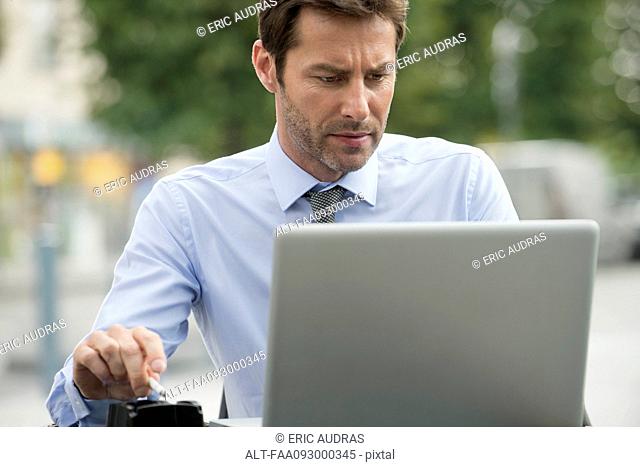 Businessman smoking while using laptop computer outdoors