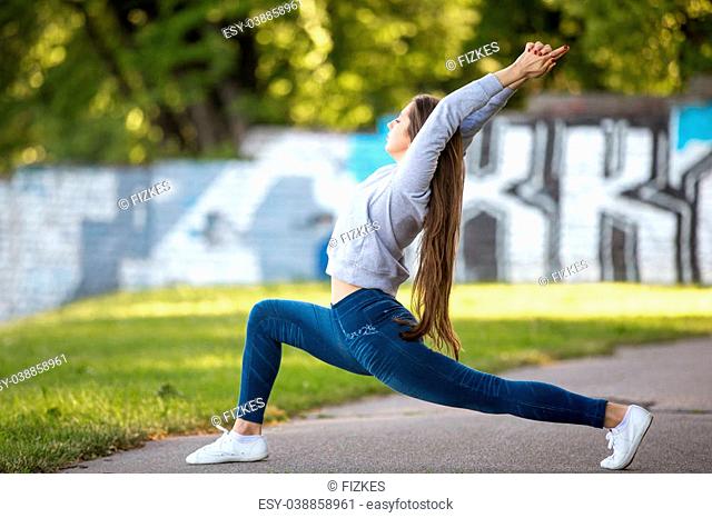 Profile of beautiful sporty young woman working out on city street, doing warming up lunge exercise, virabhadrasana 1, warrior 1, sun salutation complex