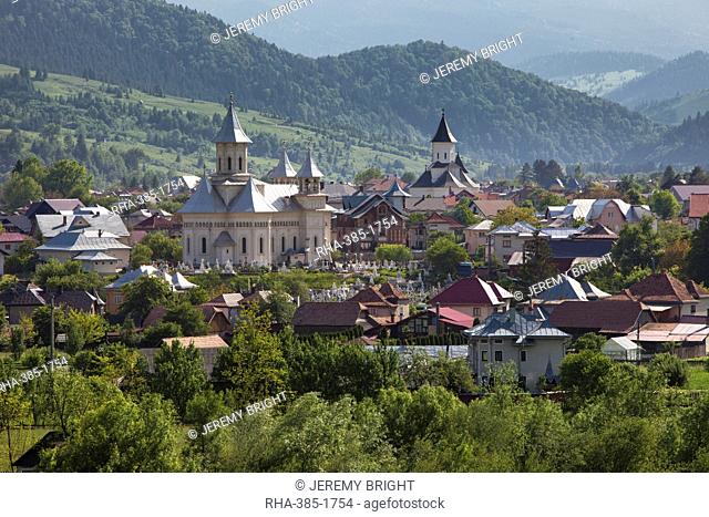 Town nestled in valley in foothills of Carpathian Mountains where churches are the dominant buildings in the village, Varma, Transylvania, Romania, Europe