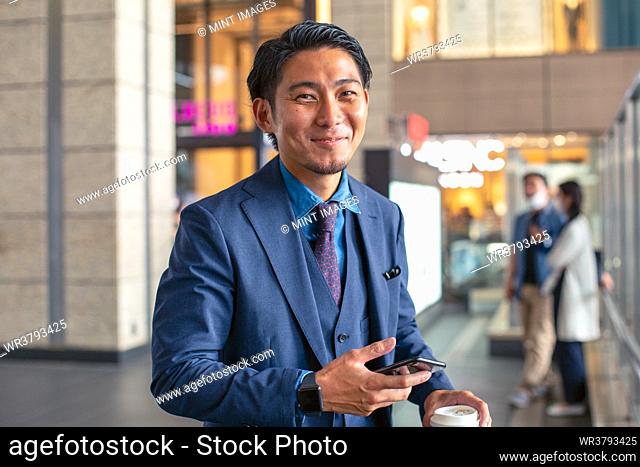 A young businessman in a blue suit on the move in a city downtown area, holding his mobile phone