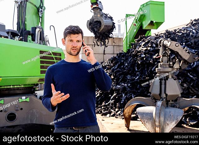 Businessman talking on smart phone in front of excavator