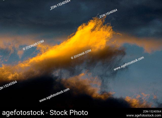 Stunning fluffy thunderstorm clouds illuminated by disappearing rays at sunset and dark thunderclouds floating across sunny blue sky to change season weather
