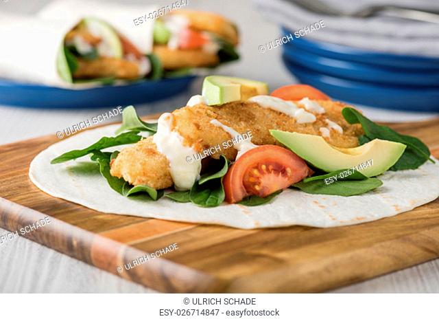 Fish finger wraps with avocado and tomato serves on wooden cheese platter