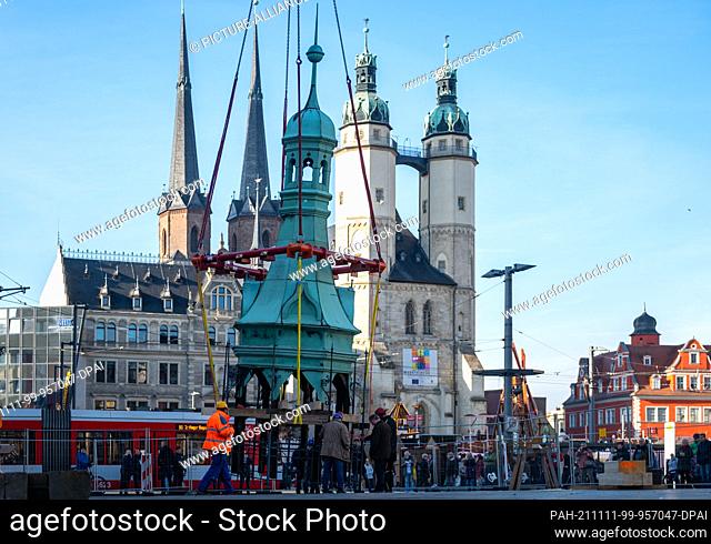 11 November 2021, Saxony-Anhalt, Halle (Saale): The spire of the town house in Halle/Saale hovers on the crane hook in front of the towers of the town church...