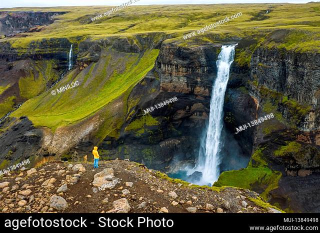 Aerial view of man standing on the cliff edge enjoying Iceland highland valley and Haifoss waterfall