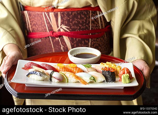 A woman wearing a kimono holding a tray of sushi