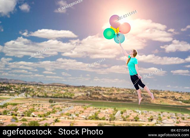 Young girl being carried up and away by balloons that she is holding above the town below