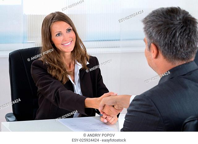 Happy Businesswoman Shaking Hands With Businessman In Office