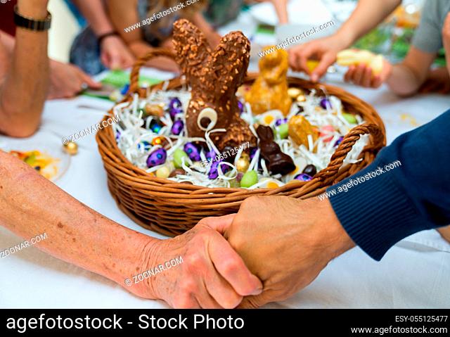 grandmother joins hands with son and gives thanks during Easter with a large Easter egg basket filled with candy and many relatives behind