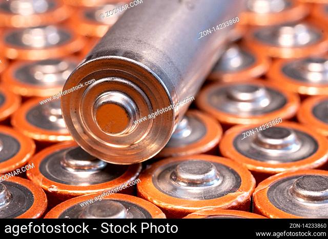Multiple used AA alkaline batteries are seen arranged in a pile. Closeup side view from the plus side of the battery. SIngle silver battery
