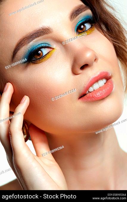 Portrait of young woman on gray background. Female posing with hand near face. Makeup with blue eyeshadow and yellow eyeliner