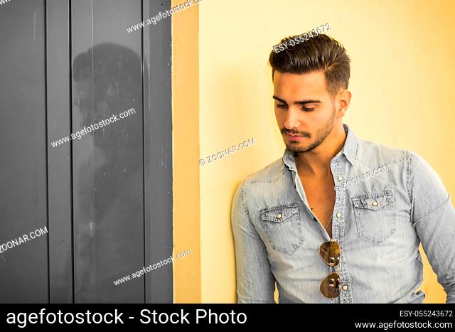 Attractive young man standing against colorful wall, looking to a side, wearing denim shirt