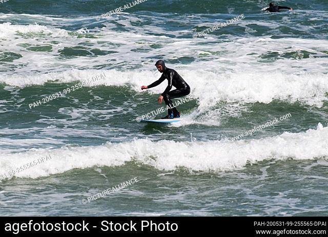 31 May 2020, Mecklenburg-Western Pomerania, Binz: Nils Miller jumps with his surfboard over waves in the Baltic Sea. Lively northeast wind has brought joy to...