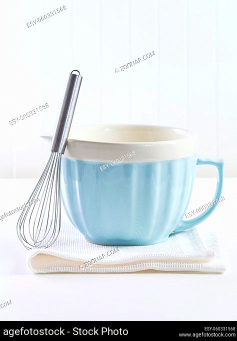 Blue mixing bowl with wisp for baking on white background. Kitchen utensil for cooking and baking