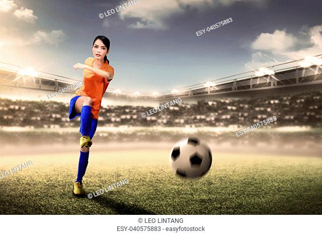 Attractive asian footballer woman kicking ball during match on stadium