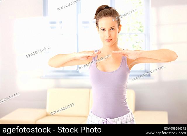 Pretty woman wearing pyjama doing morning training at home, smiling at camera