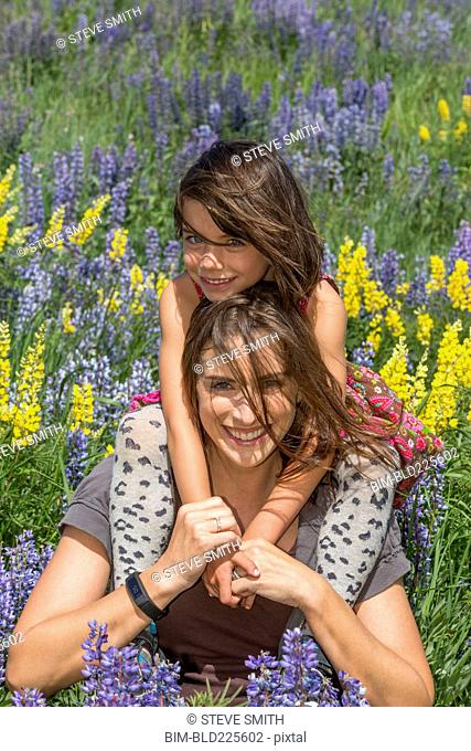 Caucasian mother carrying daughter on shoulders in wildflowers