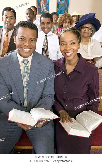 Young couple with Bibles sitting on church pews portrait