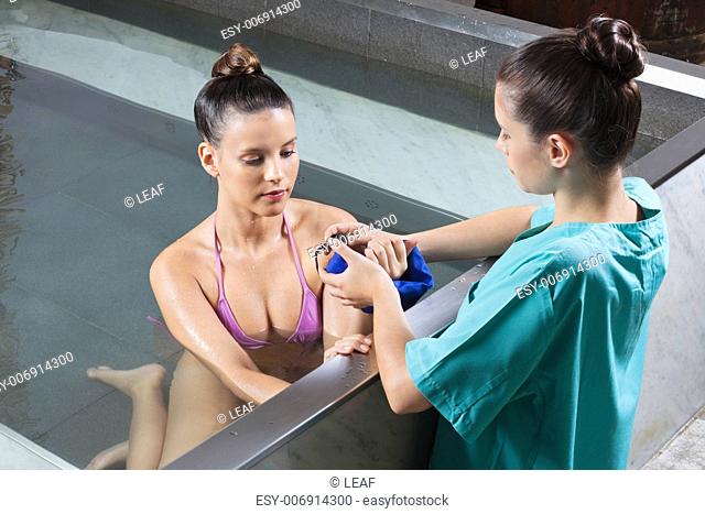 Female therapist assisting woman helping with blue belt for aqua aerobics