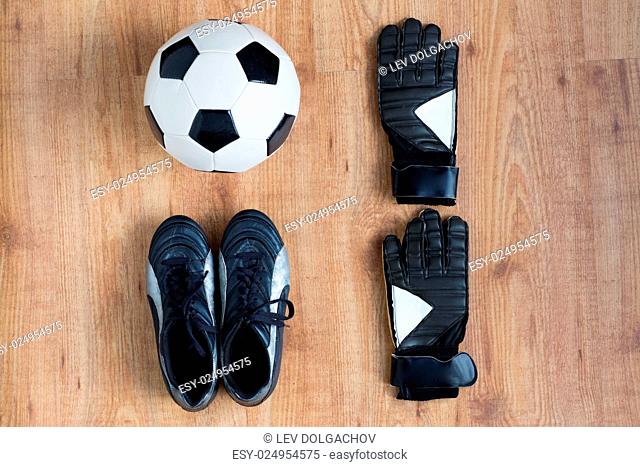 sport, soccer, football and sports equipment concept - close up of ball, boots and goalkeeper gloves on wooden background