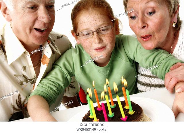 Close-up of a granddaughter blowing out candles on a birthday cake with her grandparents