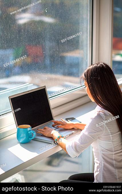 Businesswoman working in front of window with laptop computer. Business concept. Pretty woman drinking tea or coffee. Computer with blank space for your ideas