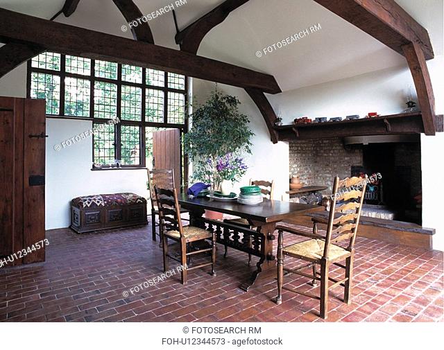 Rush-seated ladderback chairs and Arts+Crafts table in white country dining room with tiled floor and large fireplace