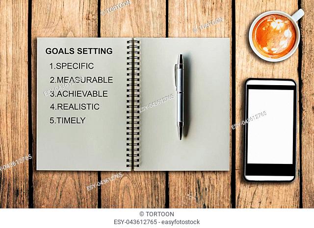 Goal setting as memo on notebook and coffee cup with mobile phone on table