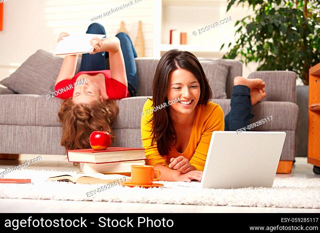 Happy teen girls studying at home in living room with books and laptop