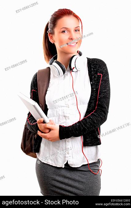 Beautiful smiling young girl in schoolgirl uniform with backpack and headphones, holding a notebook, isolated on white background