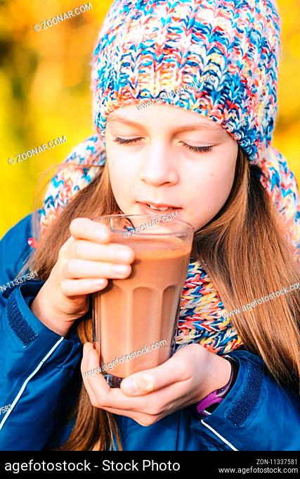 cute young girl drinking hot chocolate in a park - coziness, autumn and people concept