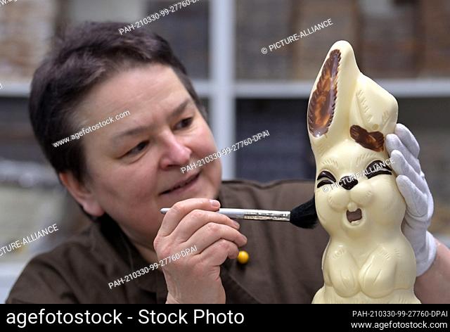 30 March 2021, Brandenburg, Himmelpfort: Sylke Wienold, head of the Himmelpforter Chocolaterie, removes disturbing particles from a bunny made of white...