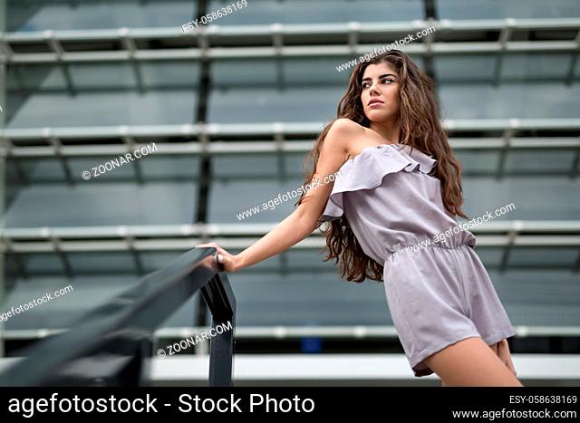 Pretty brunette with beautiful hair in the gray suit on the background of the metal-glass constructions. She holds her right hand on the black hand-rail