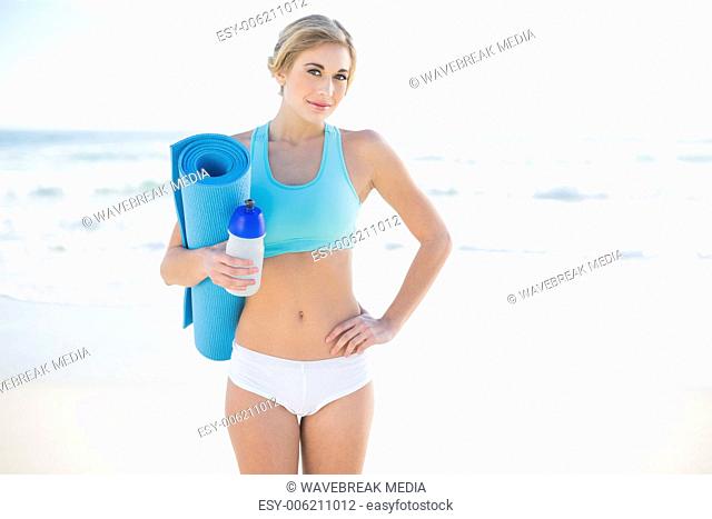 Cheerful blonde woman in sportswear carrying a bottle and an exercise mat