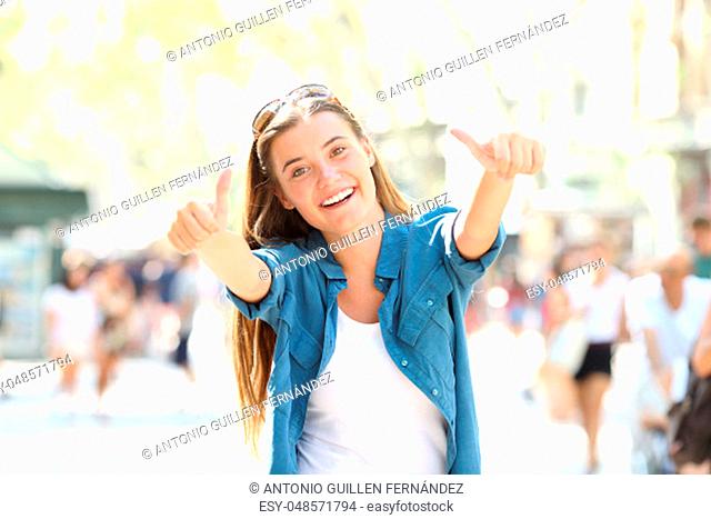 Joyful girl gesturing thumbs up looking at camera in the street
