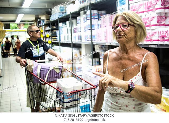 Mature retired senor caucasian woman doing her grocery shopping on vacation while her husband push the cart