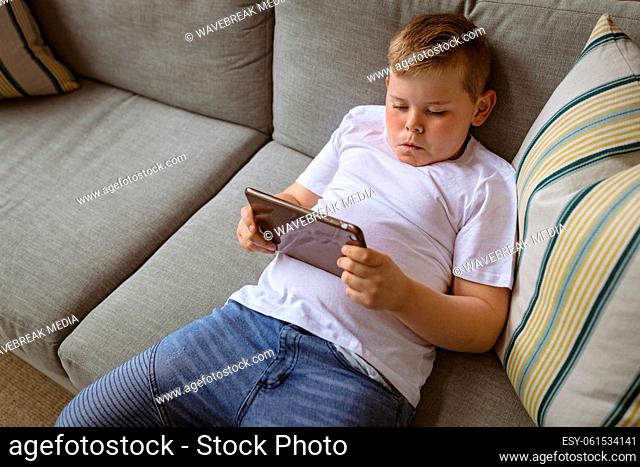 Caucasian boy using digital tablet sitting on the couch at home