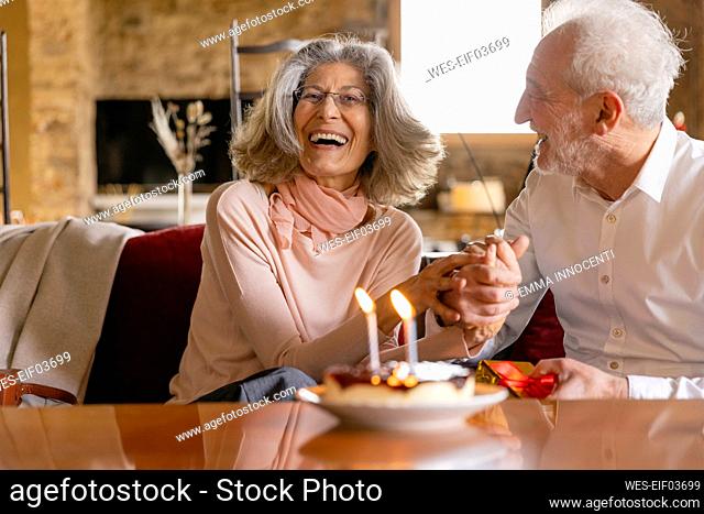 Happy senior couple with cake celebrating birthday in boutique hotel