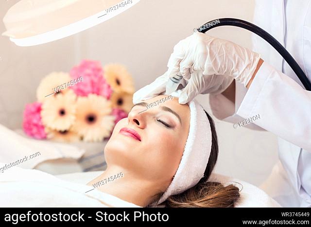 Close-up of the face of a beautiful woman smiling during innovative facial treatment for rejuvenation in a beauty center with modern technology
