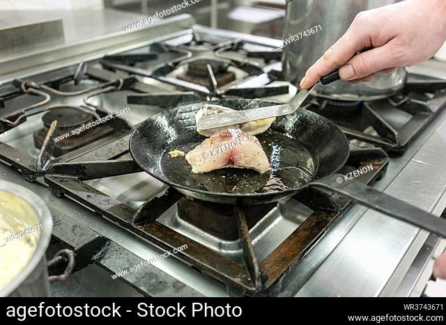 Cook or chef in Restaurant kitchen frying carp fish in pan on stove