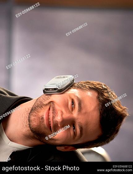 Happy young man leaning head aside, smiling, balancing mobile phone on ear