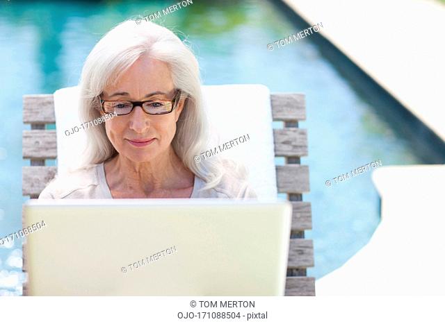 Senior woman using laptop at poolside