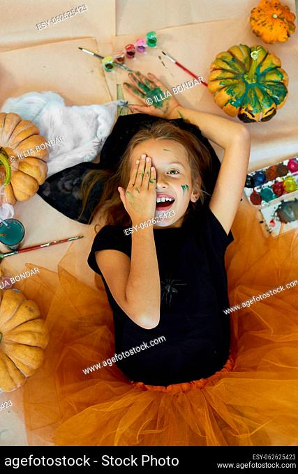 Top view of Smiling girl lying on the floor between drew pumpkin Halloween, and decoration for party, paint hands, emotion, make faces