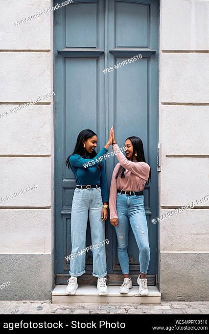 Two happy young women high fiving at a door in the city