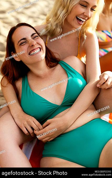 Woman wearing green bikini laughing with friend at beach