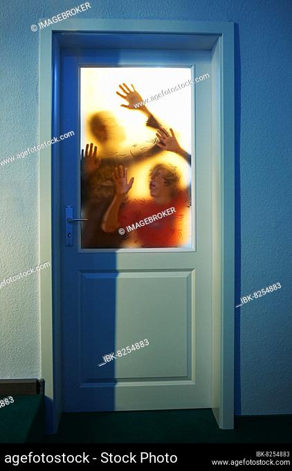 Gruselige Silhouette von zwei jungen Erwachsenen im Gegenlicht hinter einer verschlossenen Glastüre, 14 Jahre, Angst, Verzweiflung, Oberösterreich, Österreich